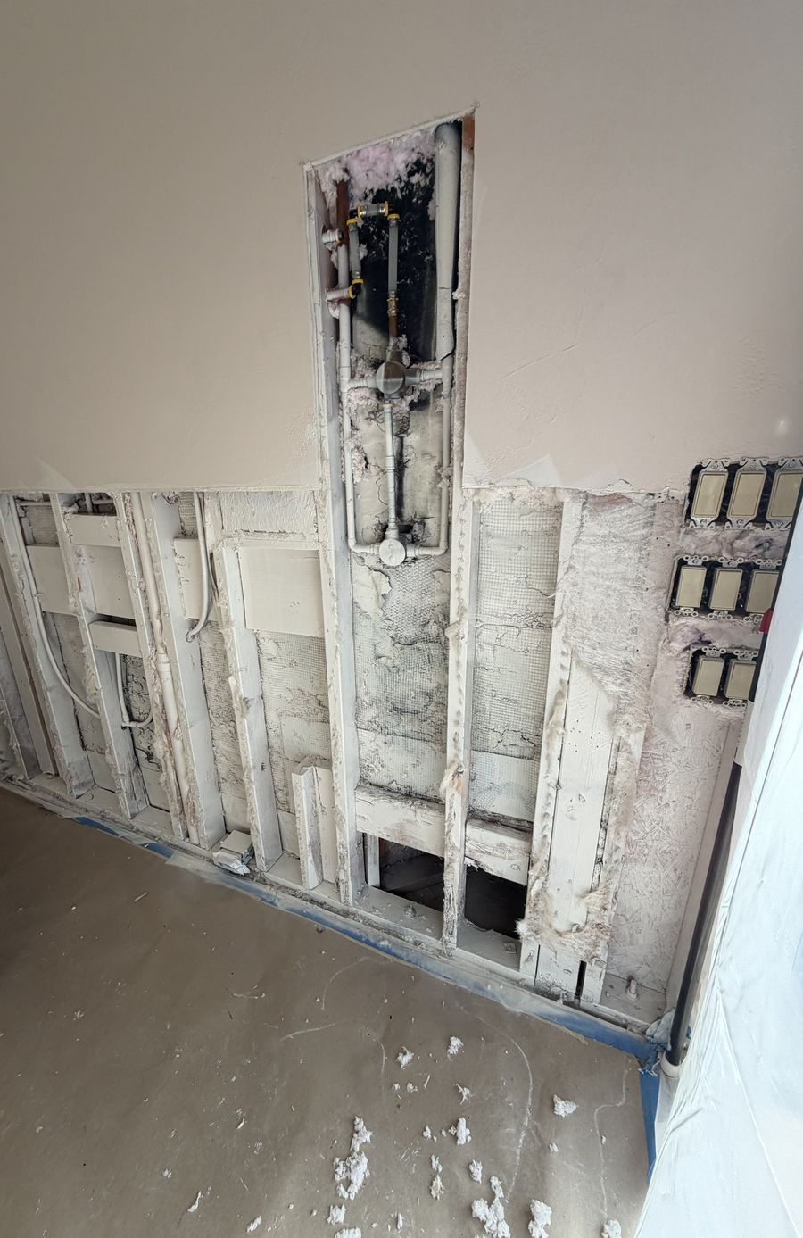 Wall opened along the bottom and up the shower valve cavity, exposing the valve, supply lines and framing